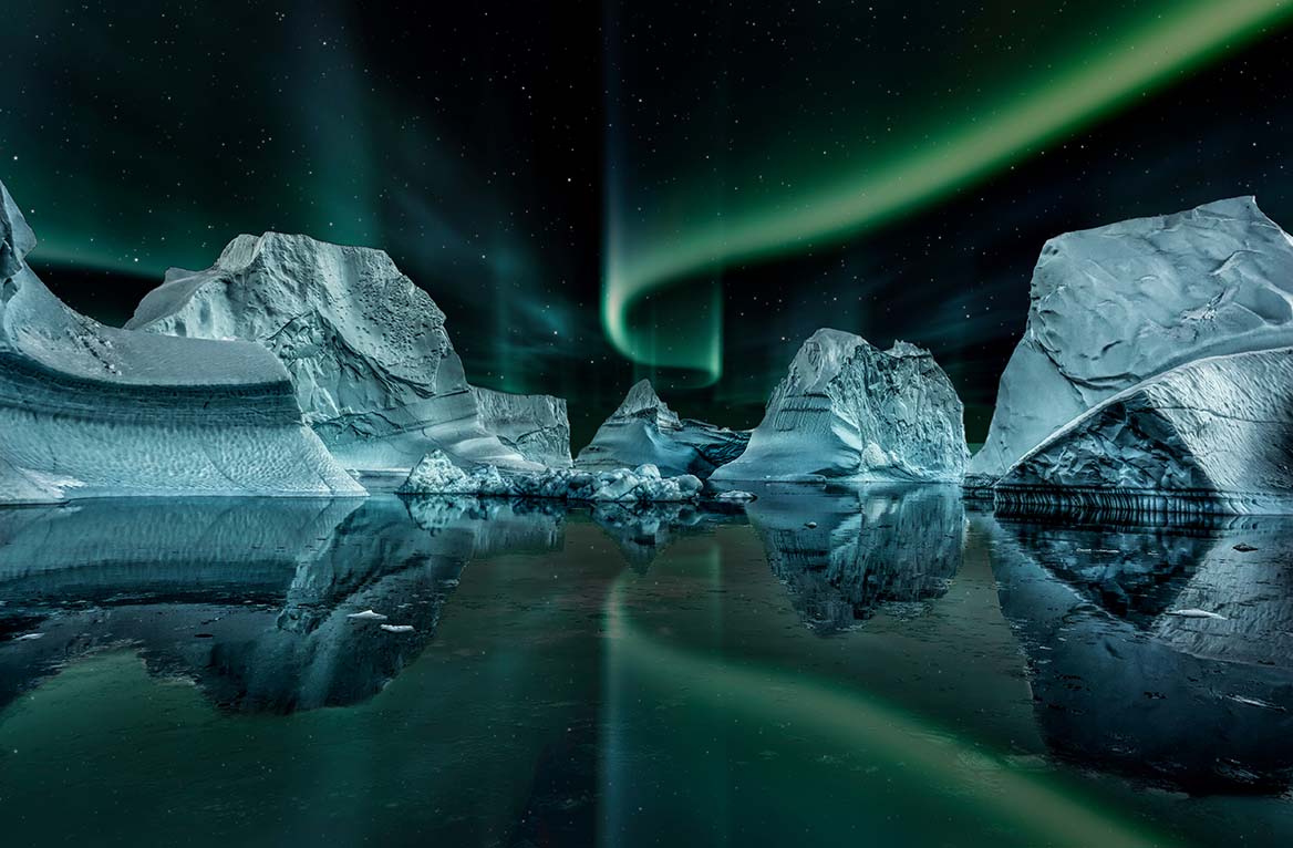 iceberg floating in greenland fjord at night with green northern lights.